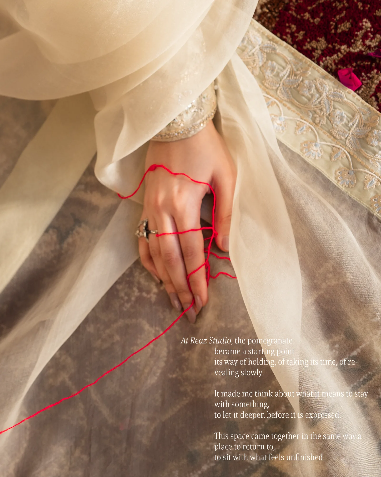A woman's hand wound with red thread against sheer cream and gold embroidery.