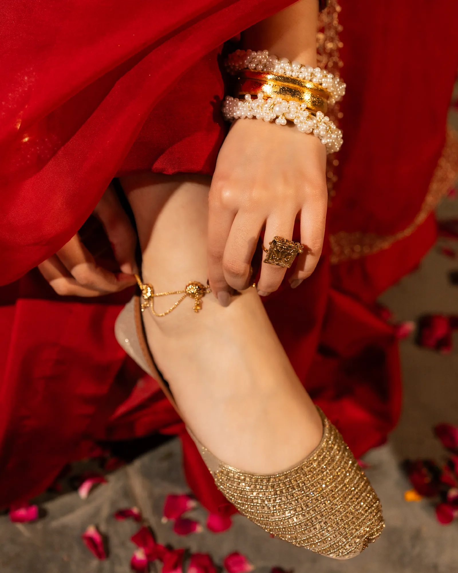 A gold khussa and anklet, a red thread at her foot among petals.