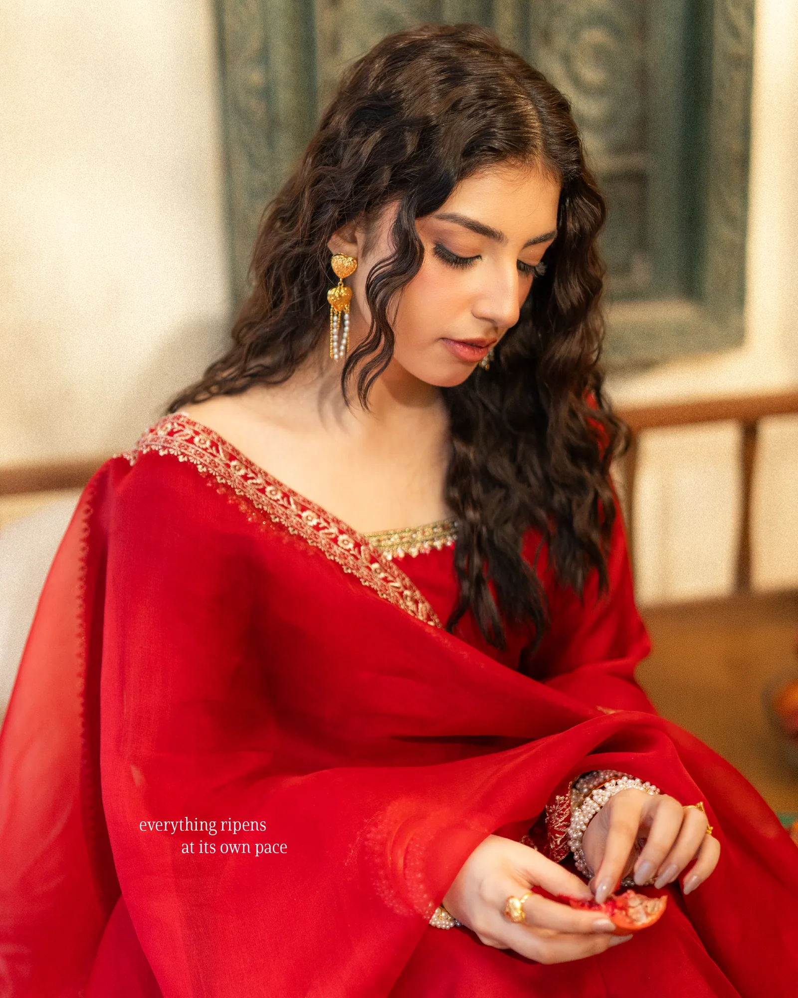 A woman in red holding a pomegranate; everything ripens at its own pace.
