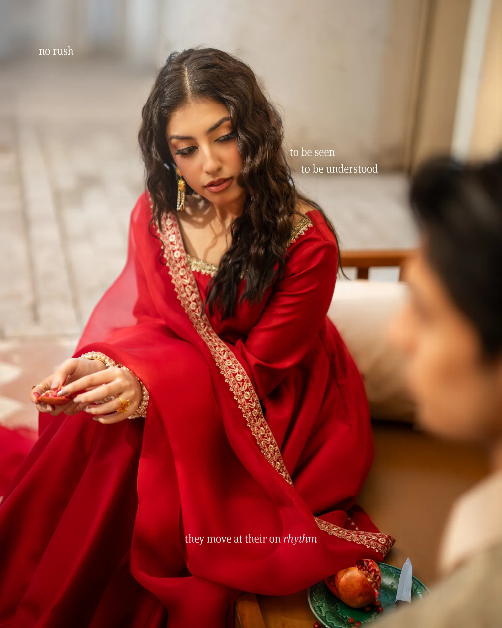 A woman in red seated, the man just at the edge of the frame; they move at their own rhythm.