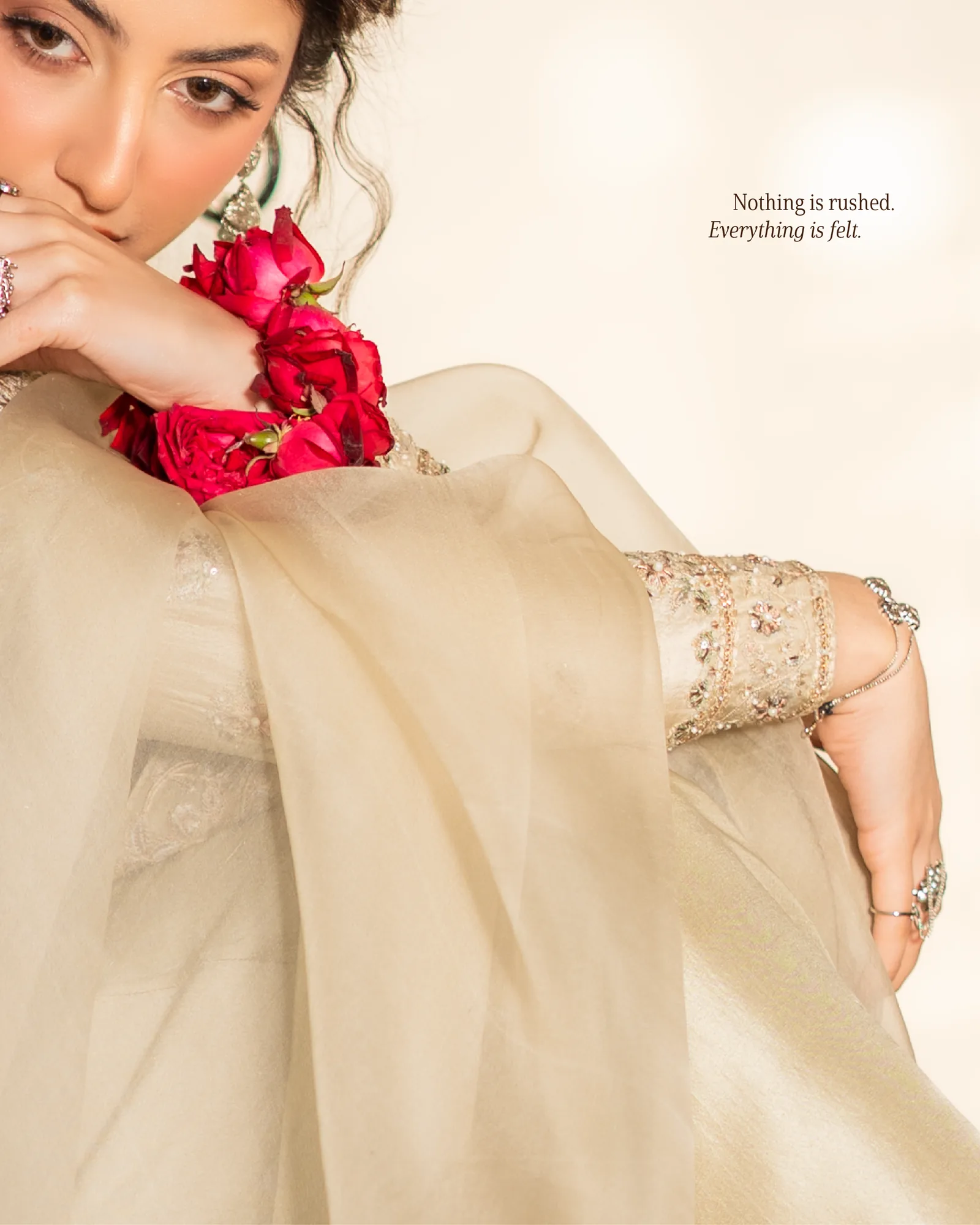 A woman in cream holding red roses to her wrist and face.