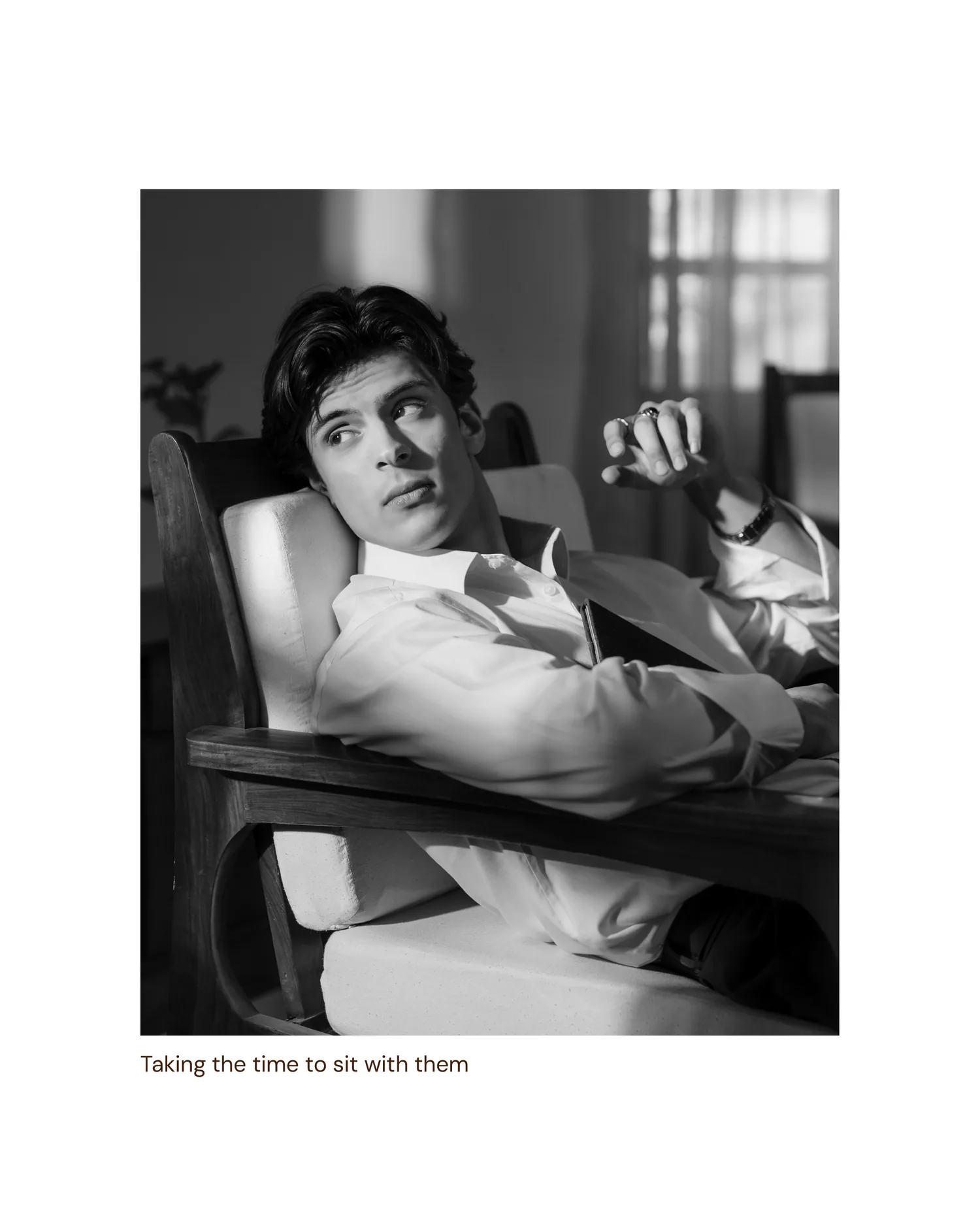 Black-and-white: the man reclining in the same wooden chair, taking his time.