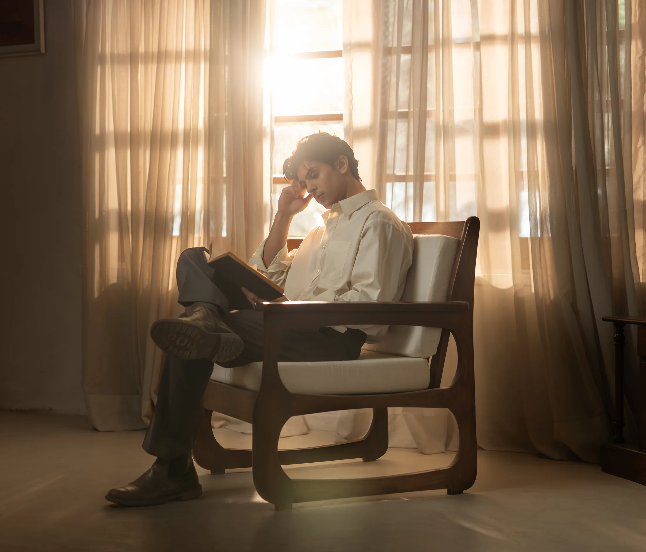 Warm, curtained interior in Lahore — a figure reading, backlit, the room and its light dominant.